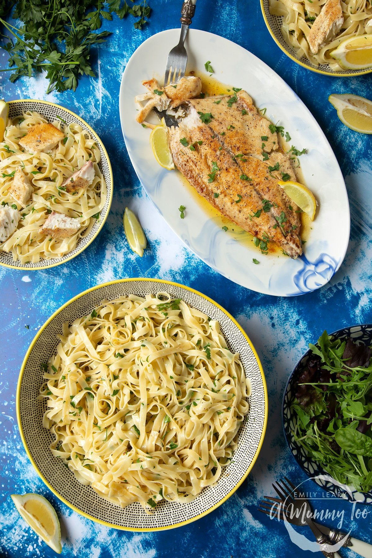 Pan-fried Yellowtail on a large oval serving dish. A fork delves into the buttery fish. A large serving bowl of herby tagliatelle is also shown.