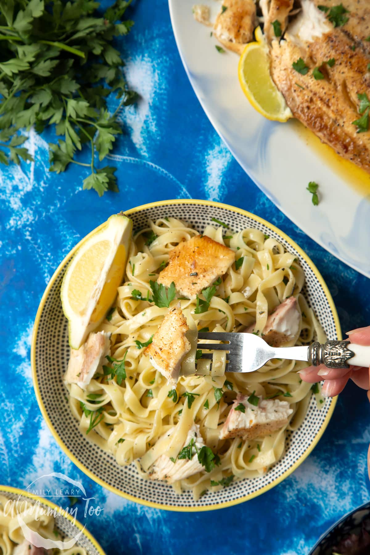 Pan-fried Yellowtail tagliatelle served in a wide, shallow bowl. A fork lifts some pasta a piece of fish from the bowl.