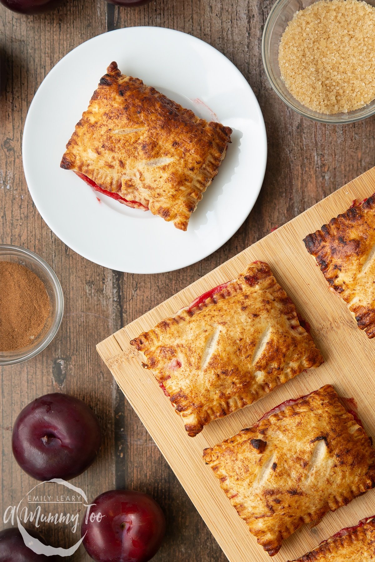 A plum pastry on white plate. More plum pastries on a wooden board.