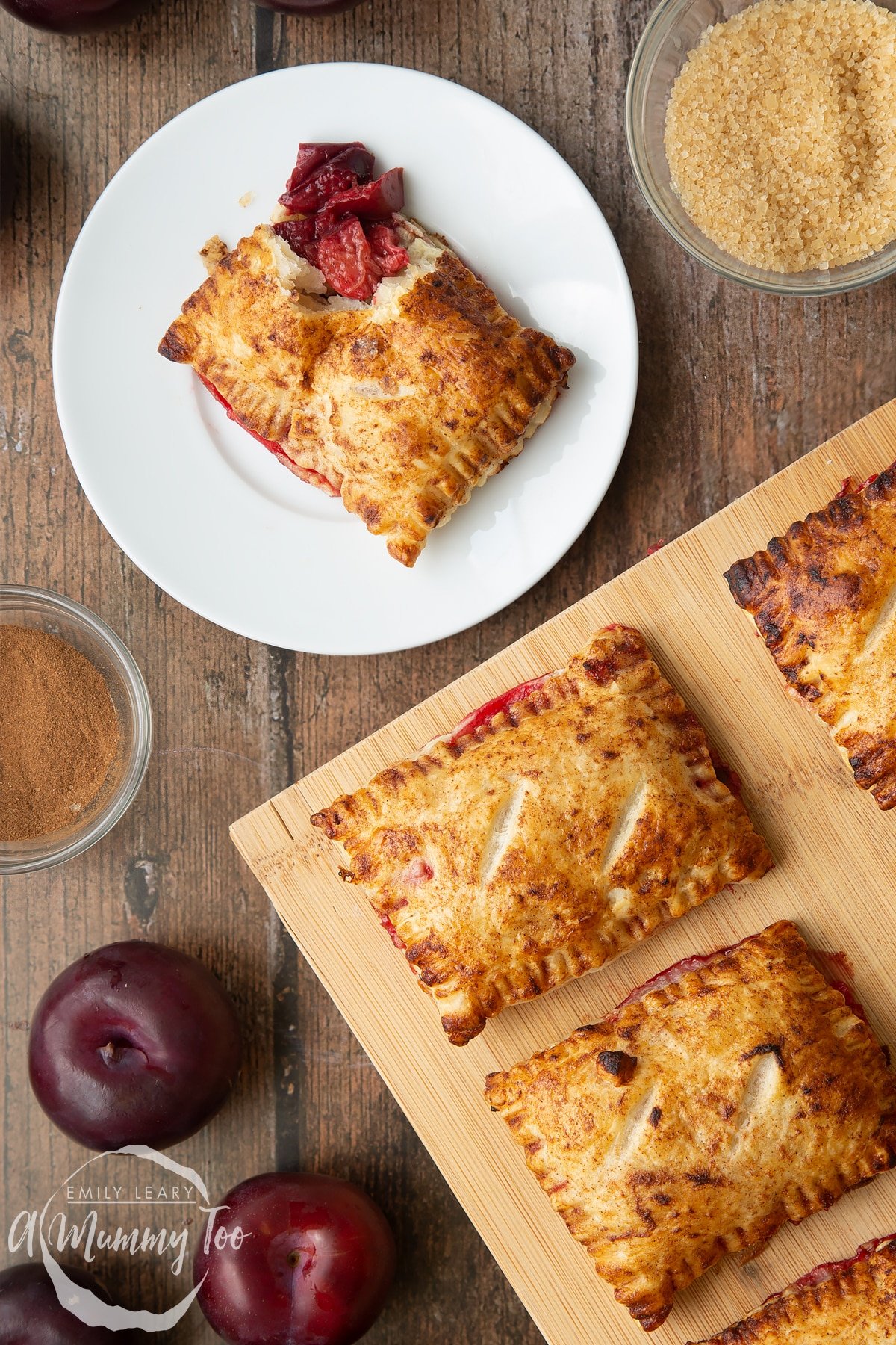 A plum pastry on white plate. The corner is broken open with the filling showing. More plum pastries on a wooden board.