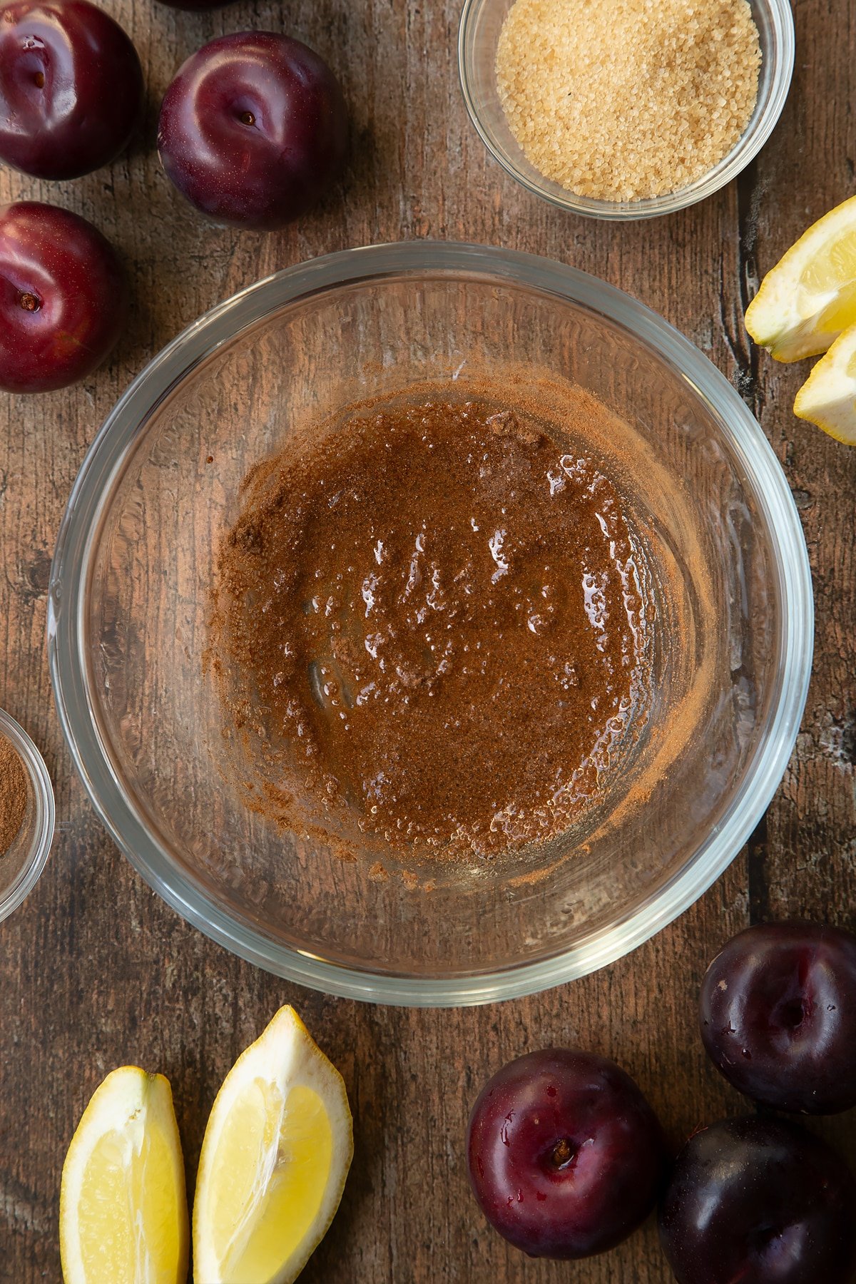 Sugar, lemon juice and cinnamon stirred together in a glass mixing bowl. Ingredients to make a plum pastry recipe surround the bowl.