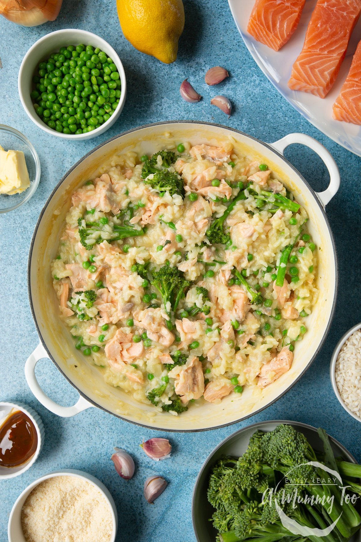 Freshly cooked salmon risotto in a large cream-colour pan. Ingredients to make salmon risotto surround the pan.