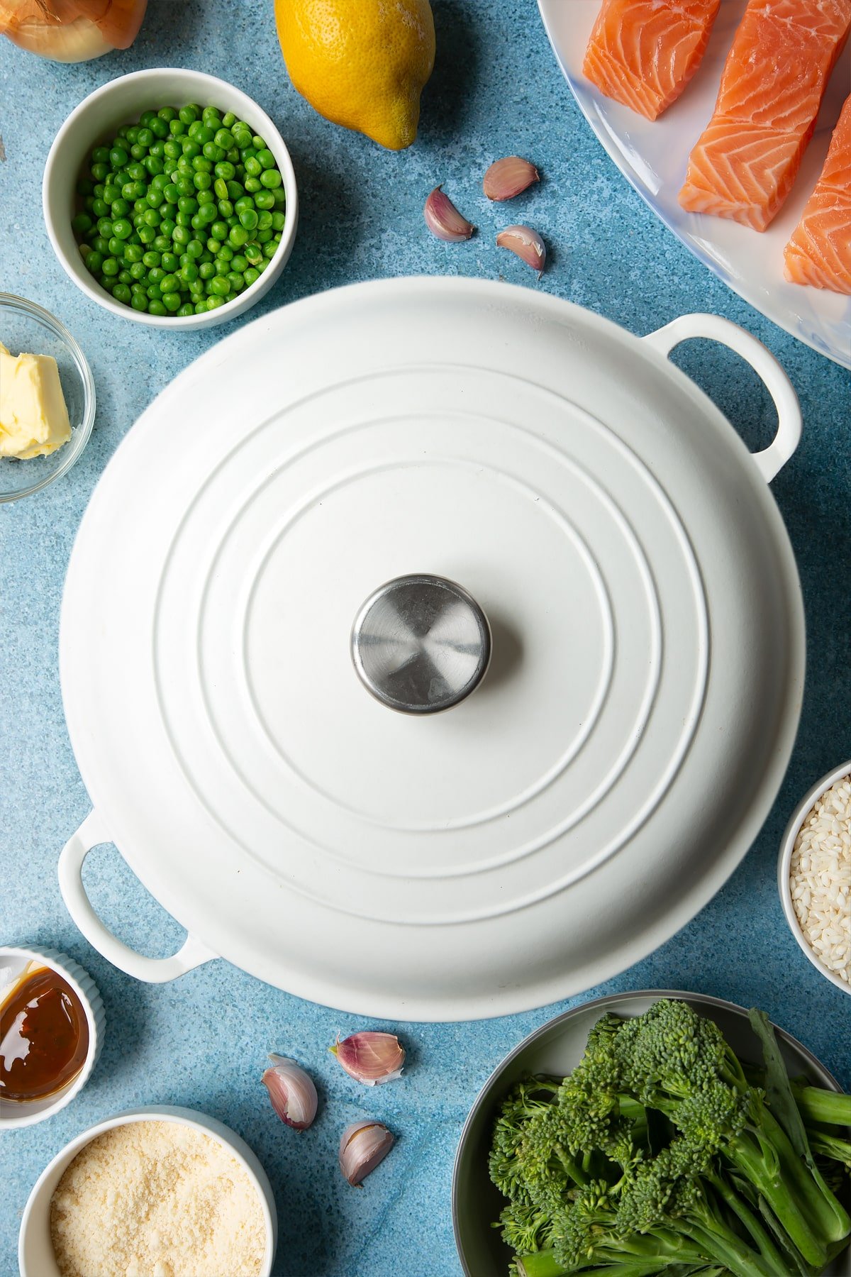 A large, lidded cream-colour pan. Ingredients to make salmon risotto surround the pan.