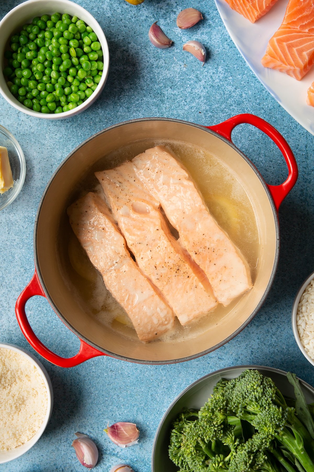Steamed salmon fillets in a red saucepan. Ingredients to make salmon risotto surround the pan.