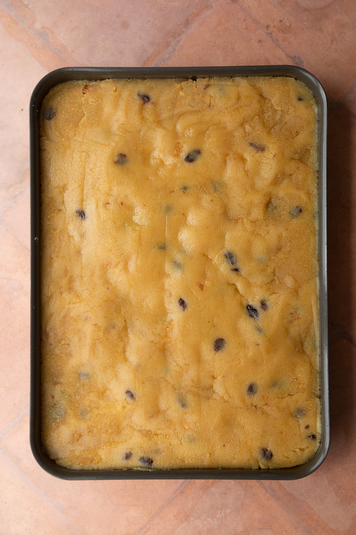 A greased tray filled with golden semolina cake dough.