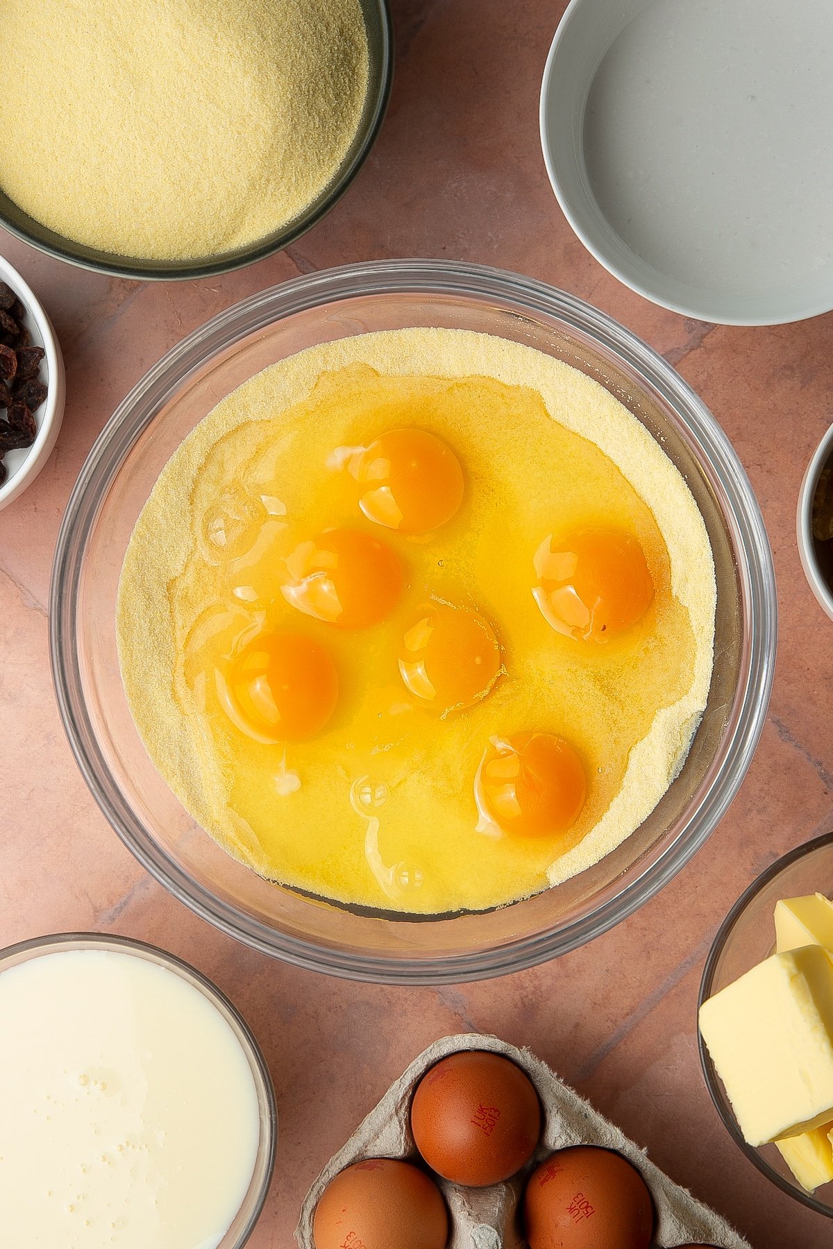 Semolina, sugar and eggs in a bowl. Ingredients to make sanwin-makin surround the bowl.
