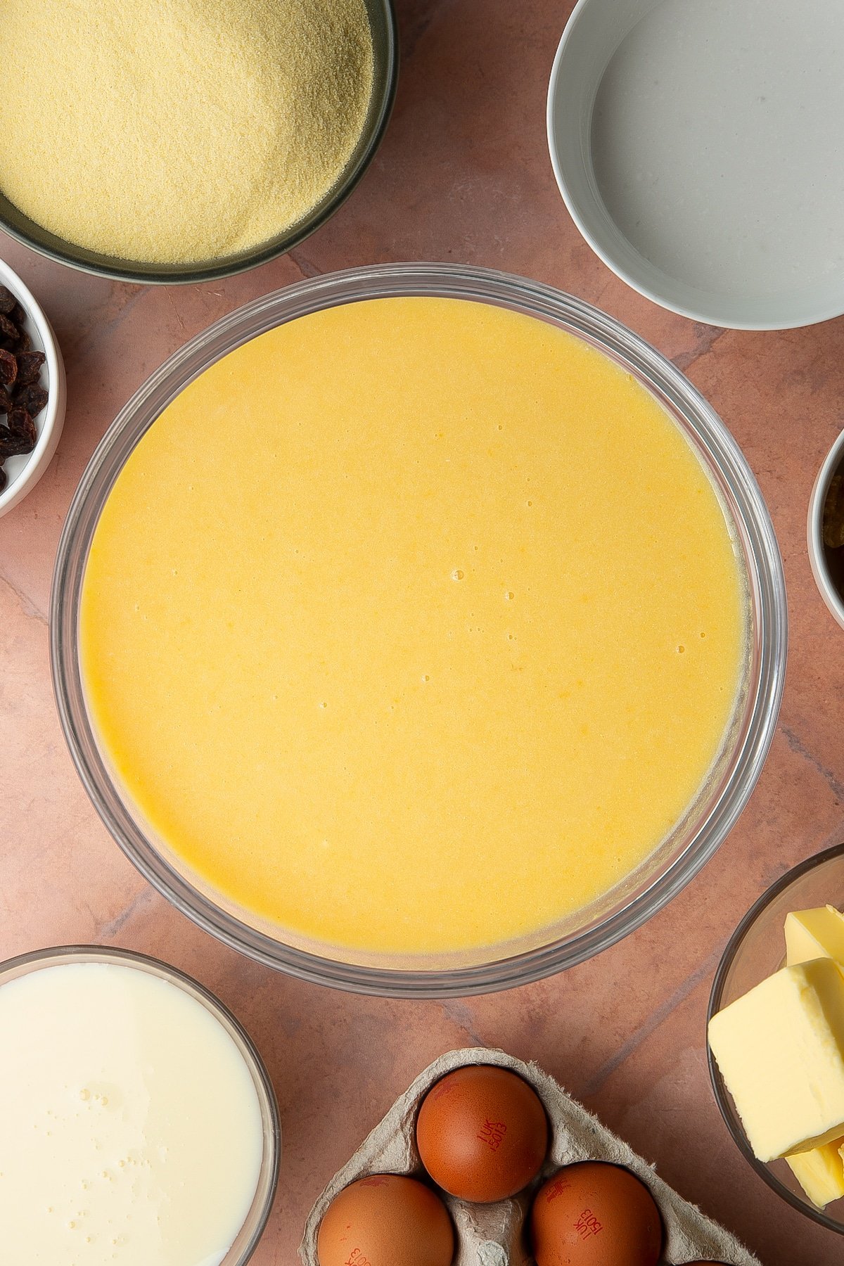 Golden semolina cake batter in a bowl. Ingredients to make sanwin-makin surround the bowl.