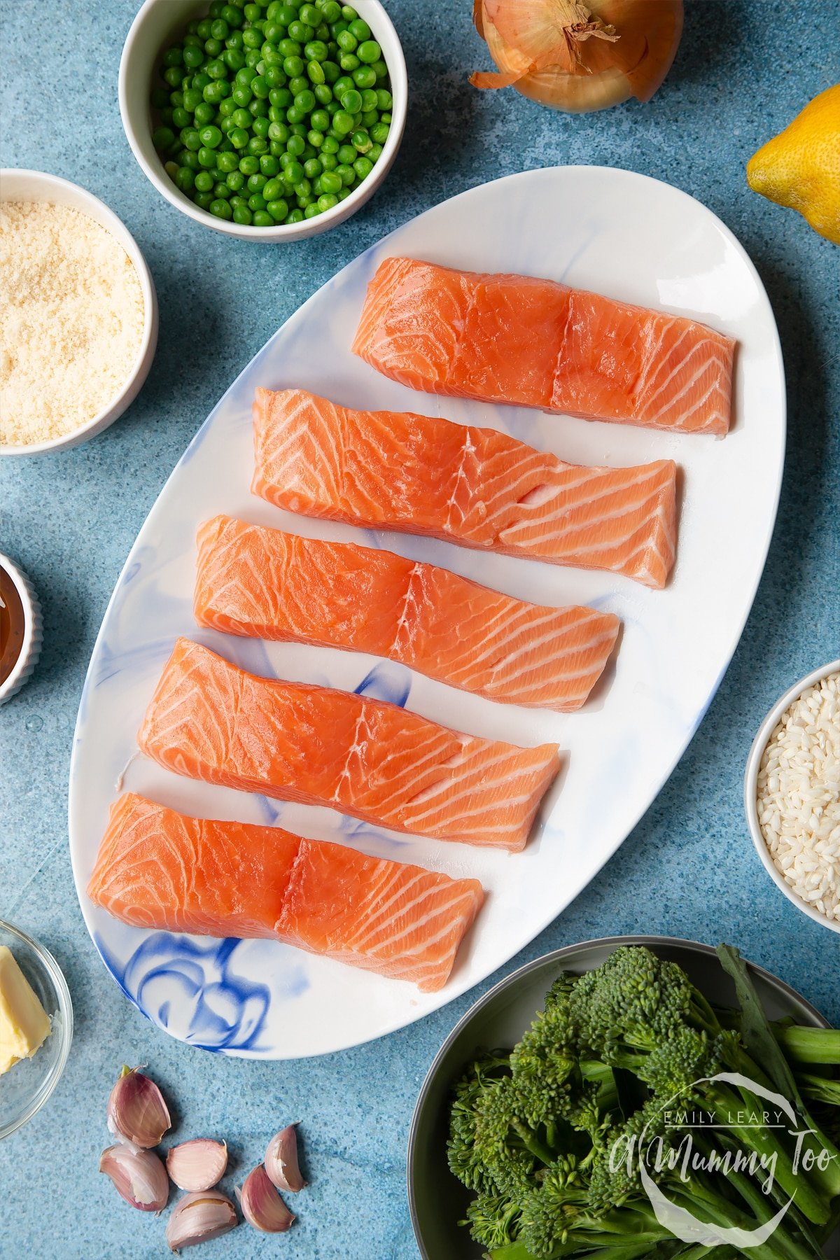 Fresh Scottish salmon fillets on a white, oval plate. Ingredients to make salmon risotto surround the plate.