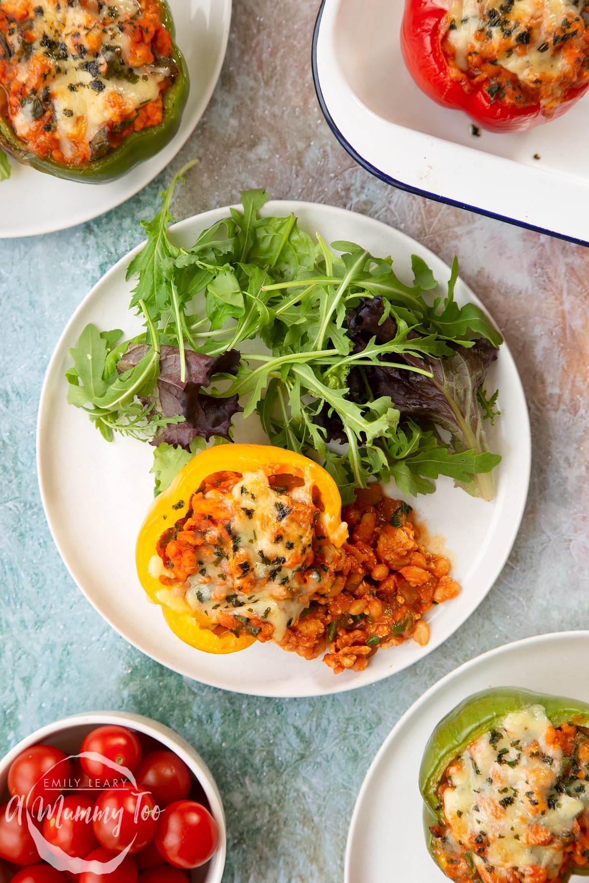 A yellow pepper stuffed with turkey mince, vegetables and baked beans with melted cheese on top. The filling spills onto the white plate. More baked bean stuffed peppers are shown to the edge of frame.