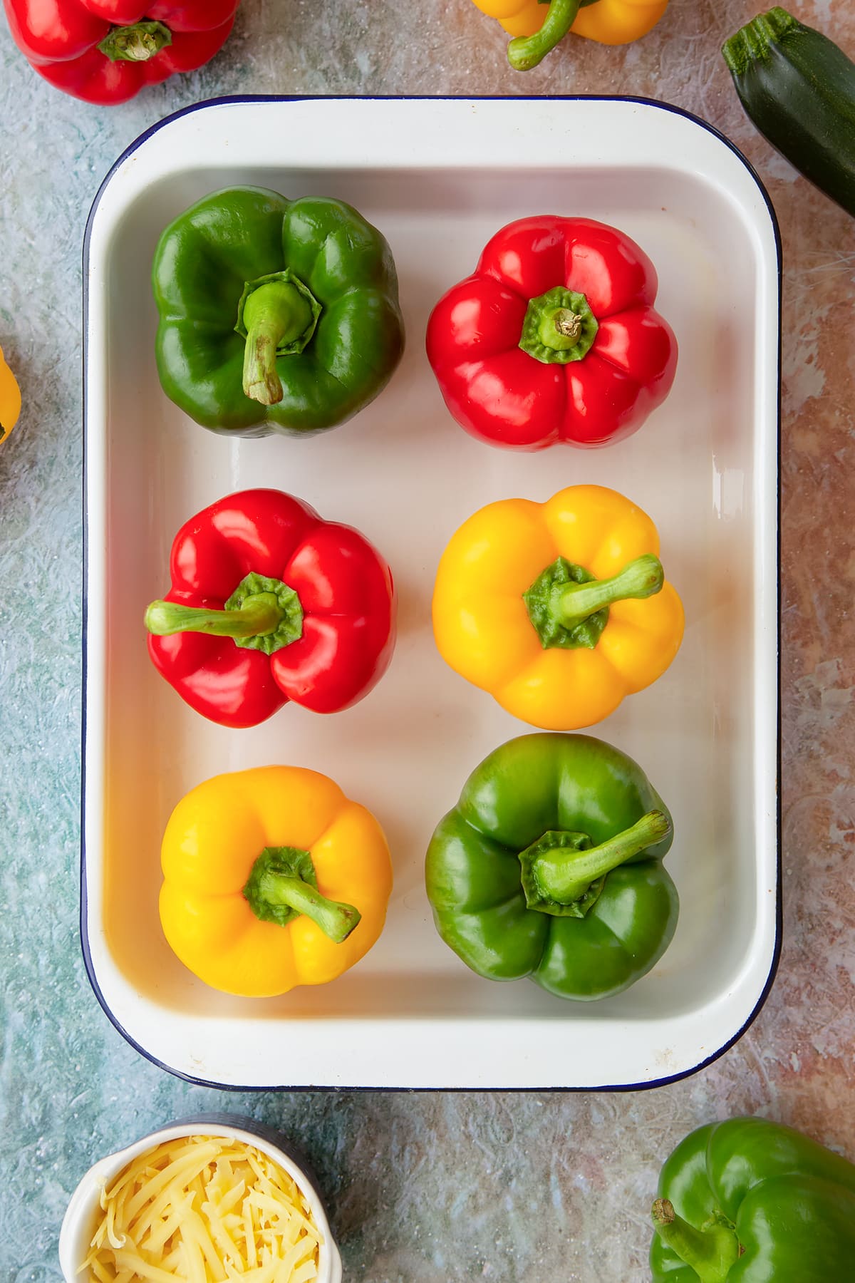 Six red, green and yellow peppers in a white roasting tray. Ingredients to make baked bean stuffed peppers surround the tray.