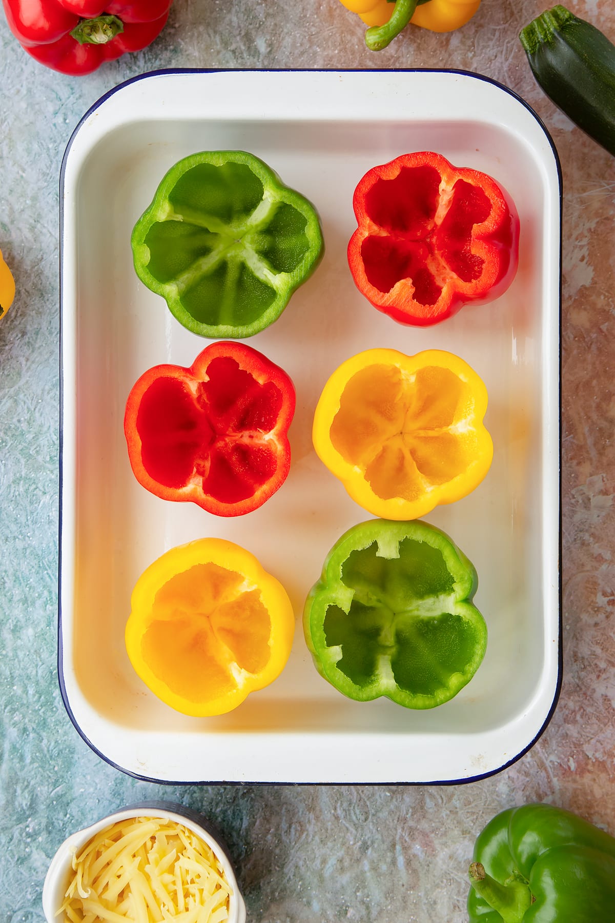 Six red, green and yellow peppers in a white roasting tray with their tops cut off and seeds removed. Ingredients to make baked bean stuffed peppers surround the tray.