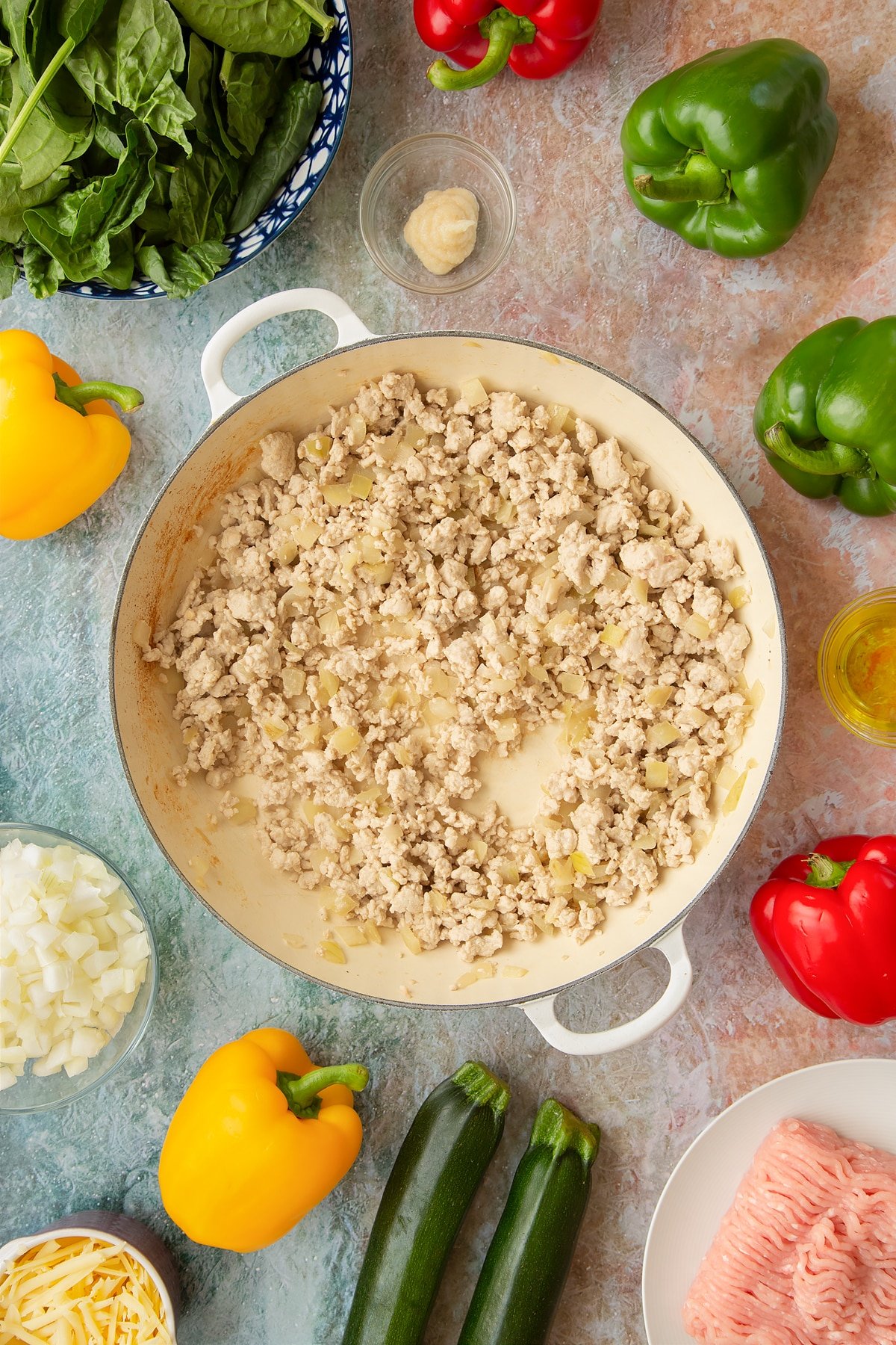 Lightly fried onions, garlic and turkey mince in a large shallow pan. Ingredients to make baked bean stuffed peppers surround the pan.