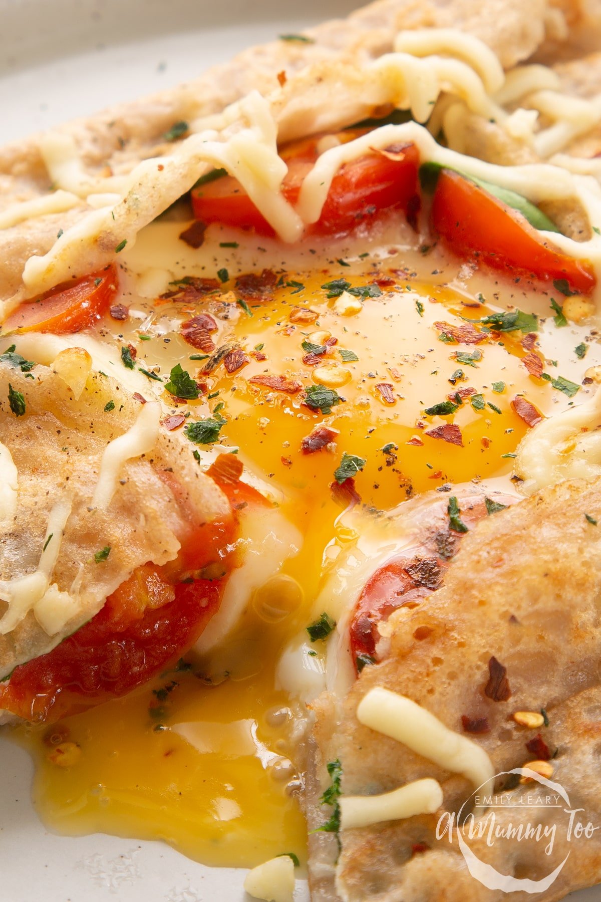 Close up of a buckwheat galette filled with spinach, tomatoes, cheese and a lightly cooked egg. The galette has been cut to reveal the custardy yolk.