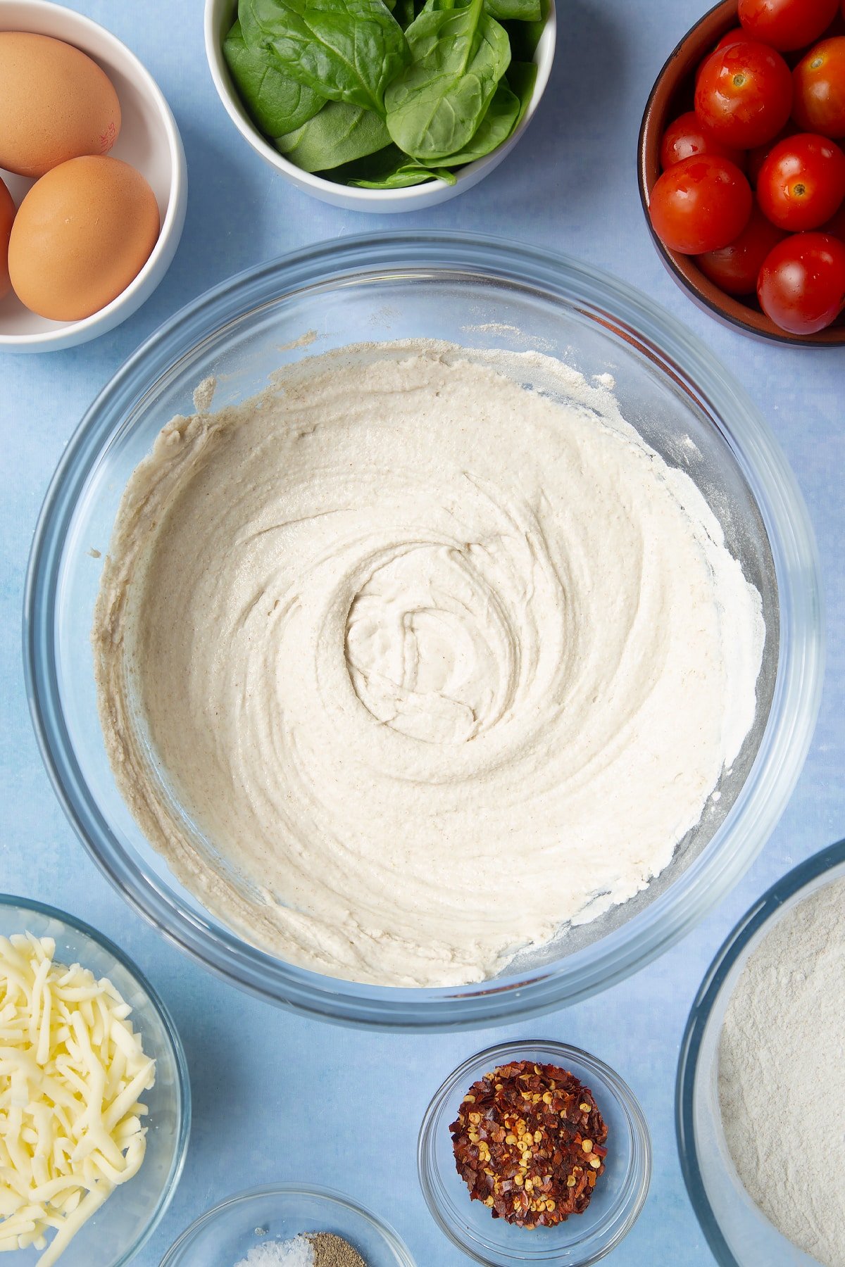 Buckwheat flour and water paste in a glass mixing bowl. Ingredients to make buckwheat galettes surround the bowl.