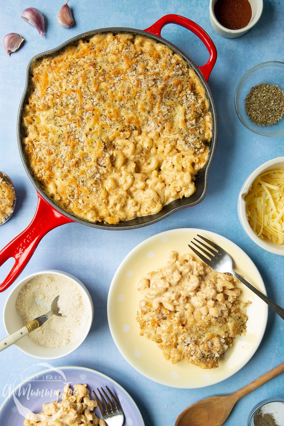 Garlic and herb mac and cheese on a yellow spotty plate with a fork. Alongside it is a skillet with more of the mac and cheese.