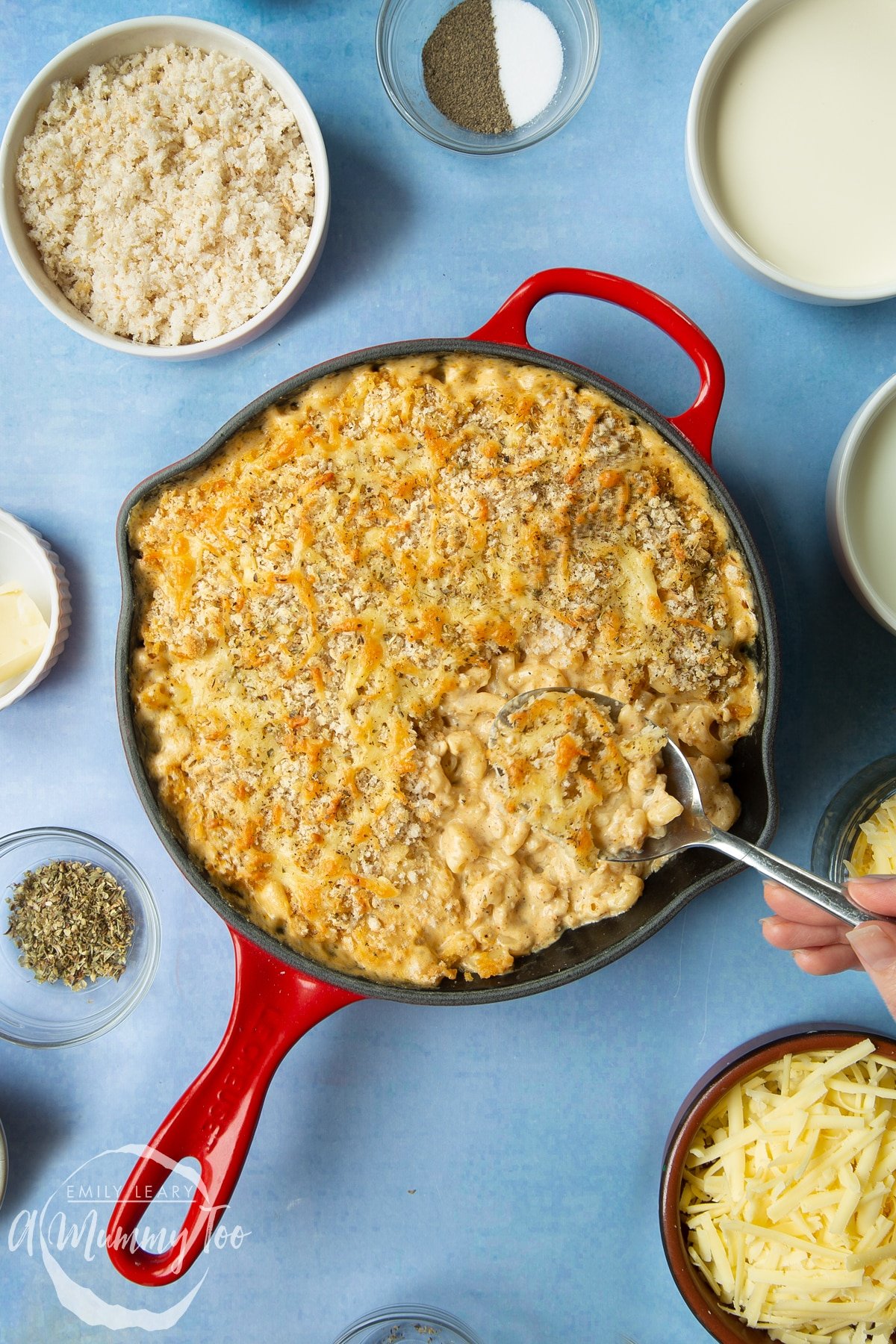 Freshly baked garlic and herb mac and cheese in a skillet. A hand holds a large spoon, delving into the skillet.