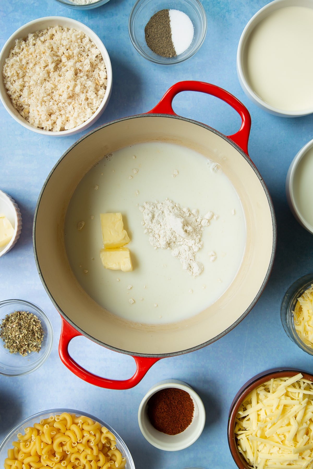 Flour, butter and milk in a pan. Ingredients to make garlic and herb mac and cheese surround the pan.