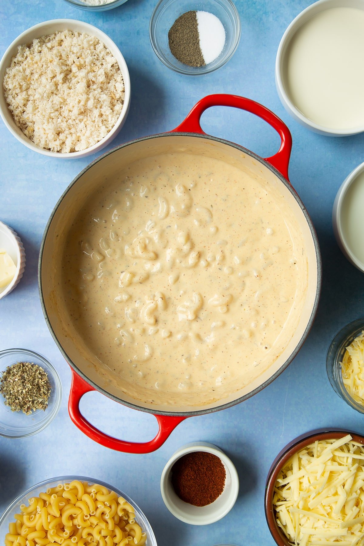 Spicy, cheesy, herby mac and cheese in a pan. Ingredients to make garlic and herb mac and cheese surround the pan.