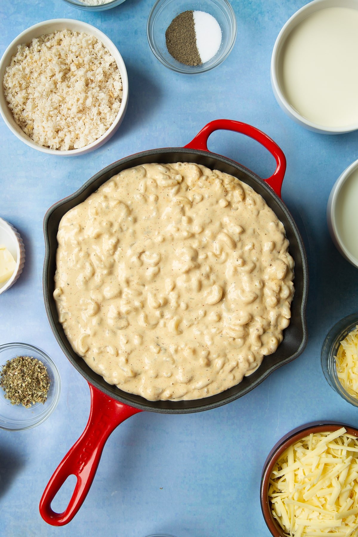 Spicy, cheesy, herby mac and cheese in a skillet. Ingredients to make garlic and herb mac and cheese surround the skillet.