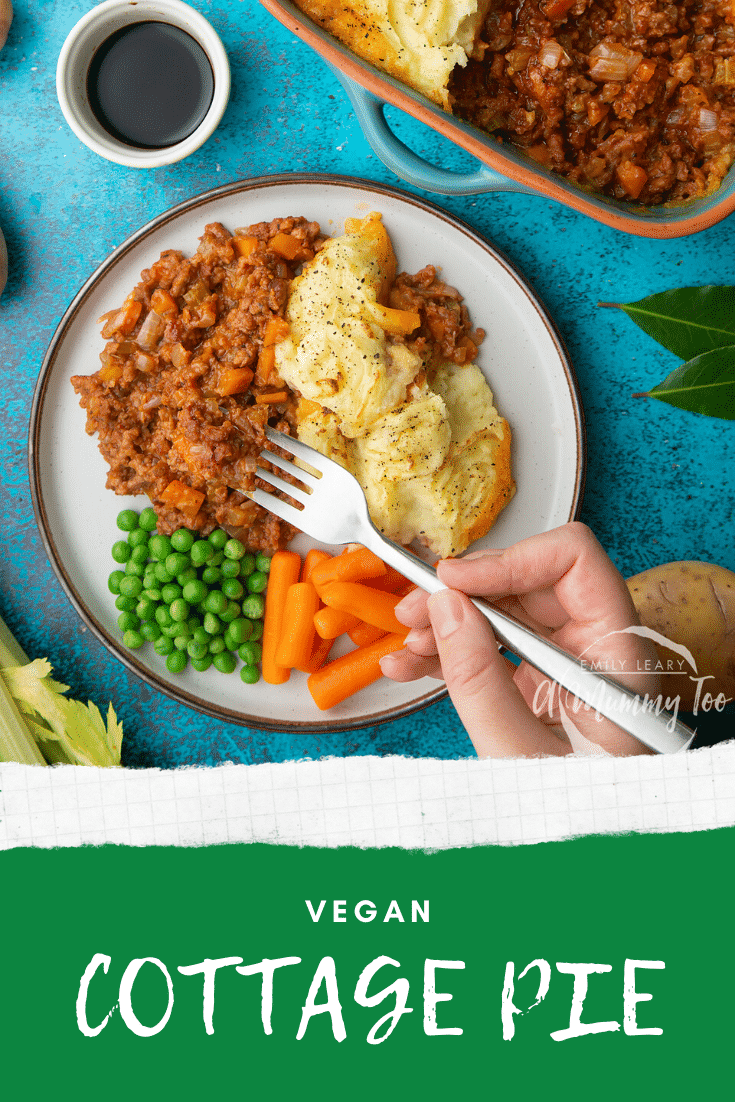 Vegan cottage pie served on a plate with peas and carrots. A hand with a fork reaches to take a bite. Caption reads: vegan cottage pie.