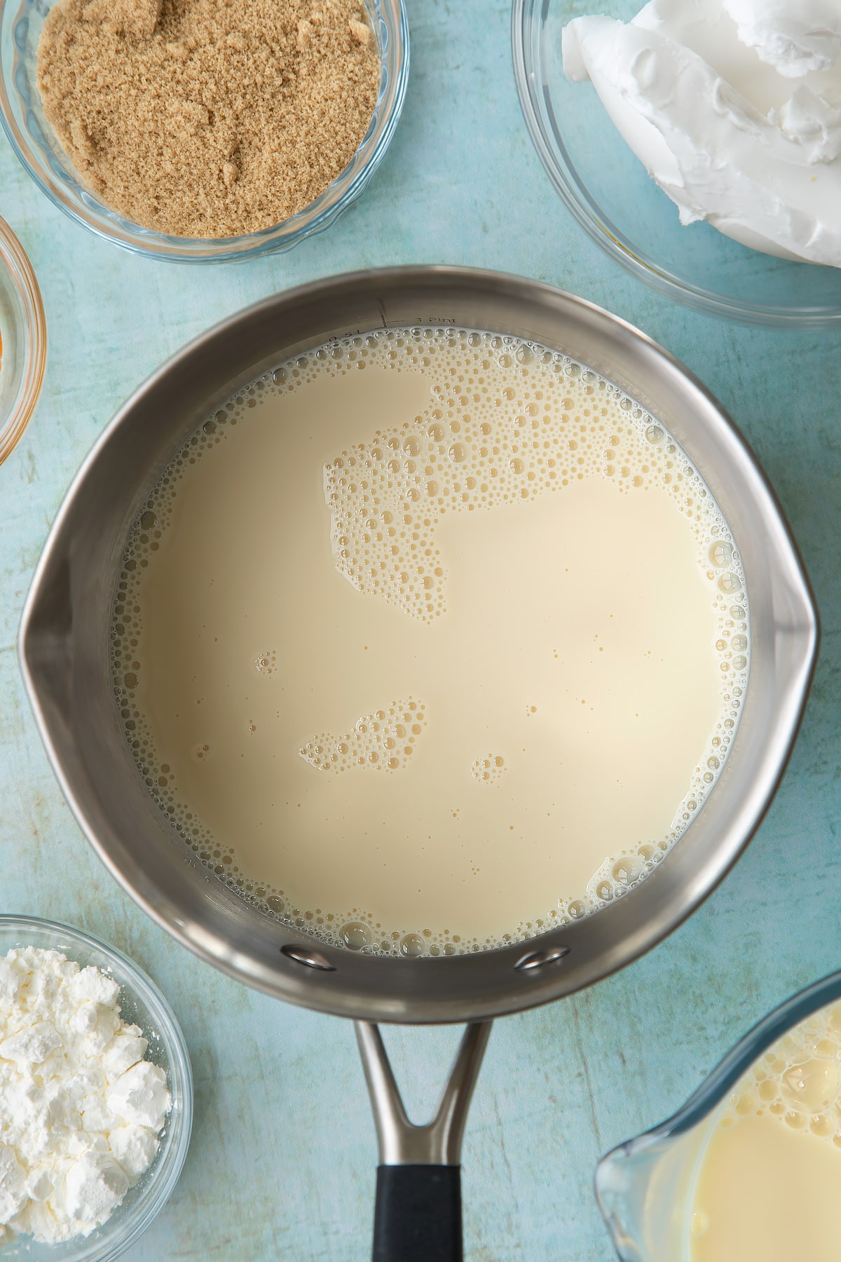 Soya milk, vanilla and sugar in a pan. Ingredients to make vegan custard surround the pan.