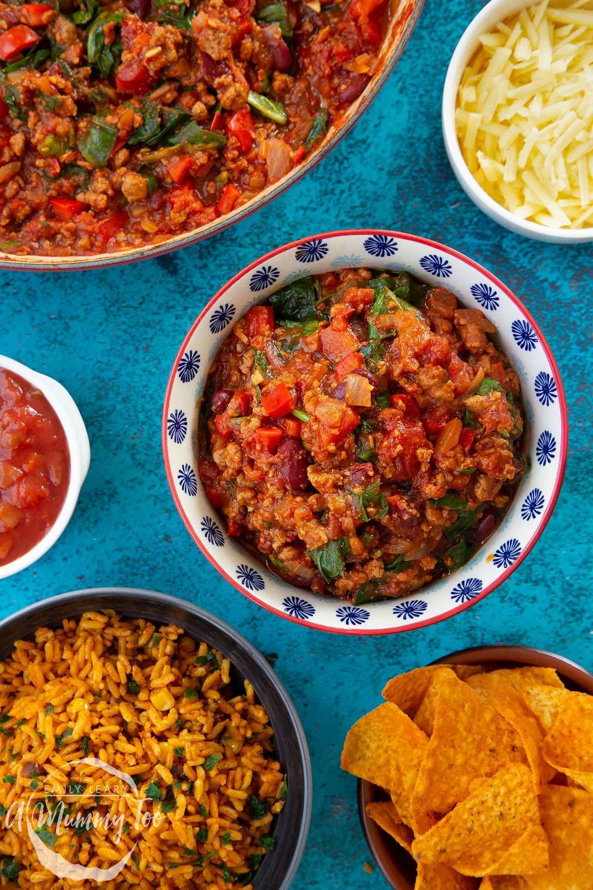 Vegetarian mince chilli in a bowl. Bowls containing tortilla chips, salsa, grated cheese and spicy rice are also shown.