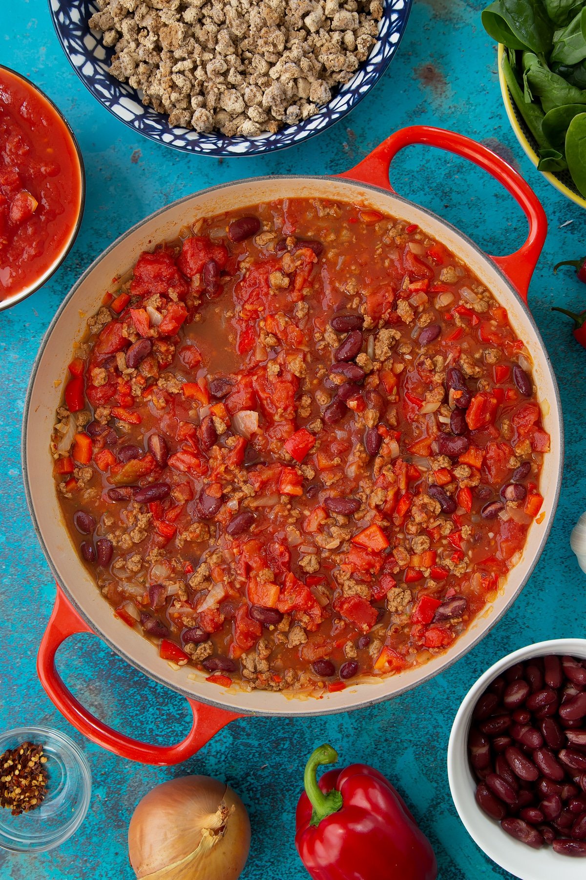 Half cooked vegetarian mince chilli in a pan. Ingredients to make vegetarian mince chilli surround the pan.
