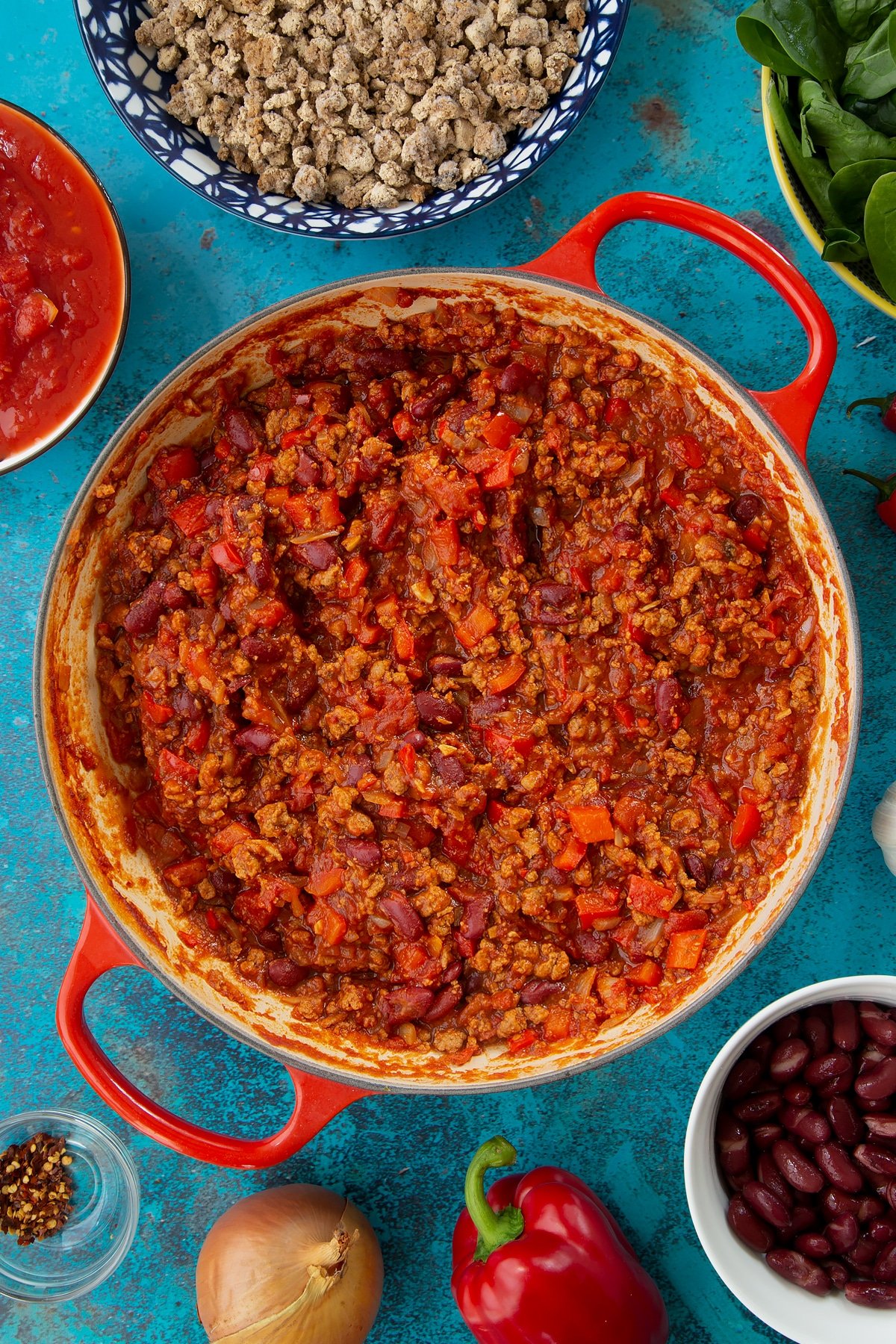 Vegetarian mince chilli in a pan, almost ready. Ingredients to make vegetarian mince chilli surround the pan.