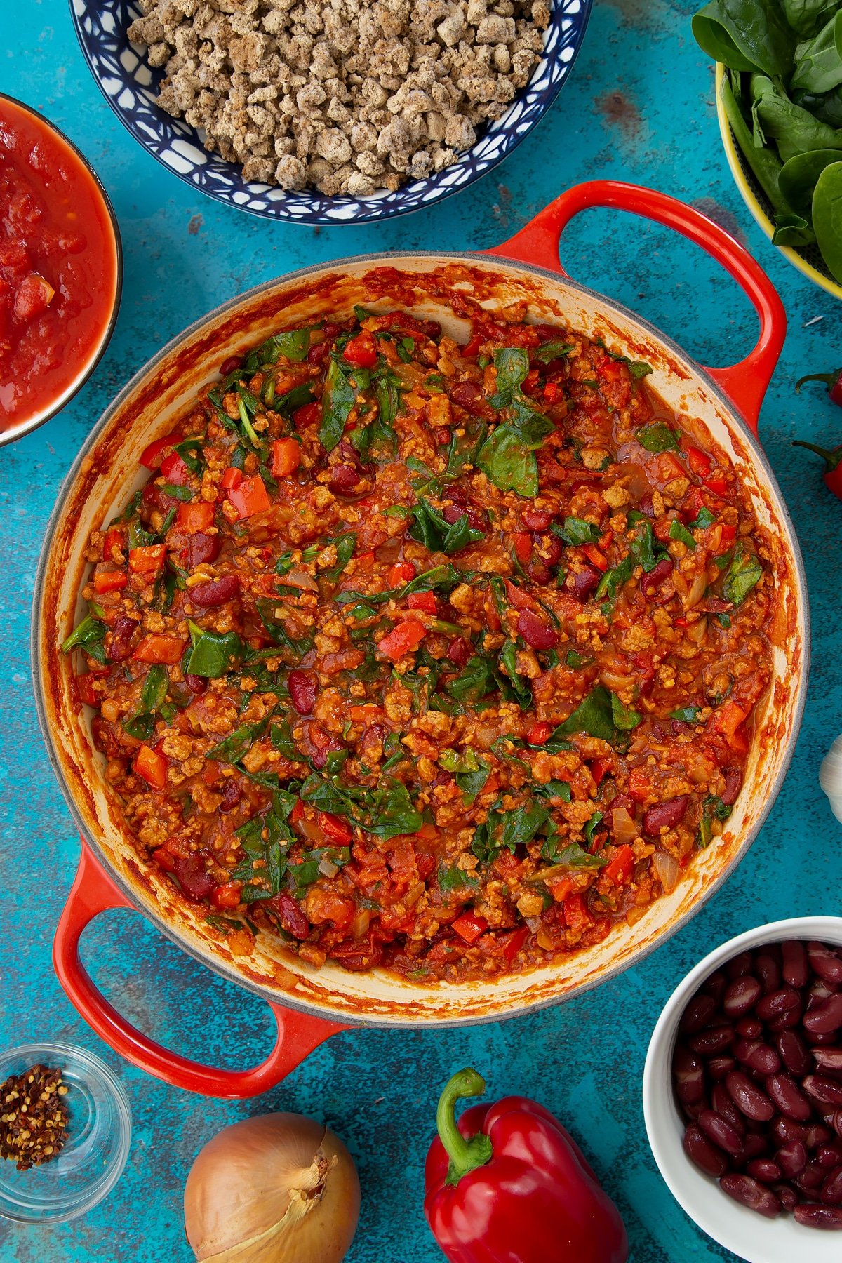 Vegetarian chilli in a pan, freshly cooked. Ingredients to make vegetarian mince chilli surround the pan.