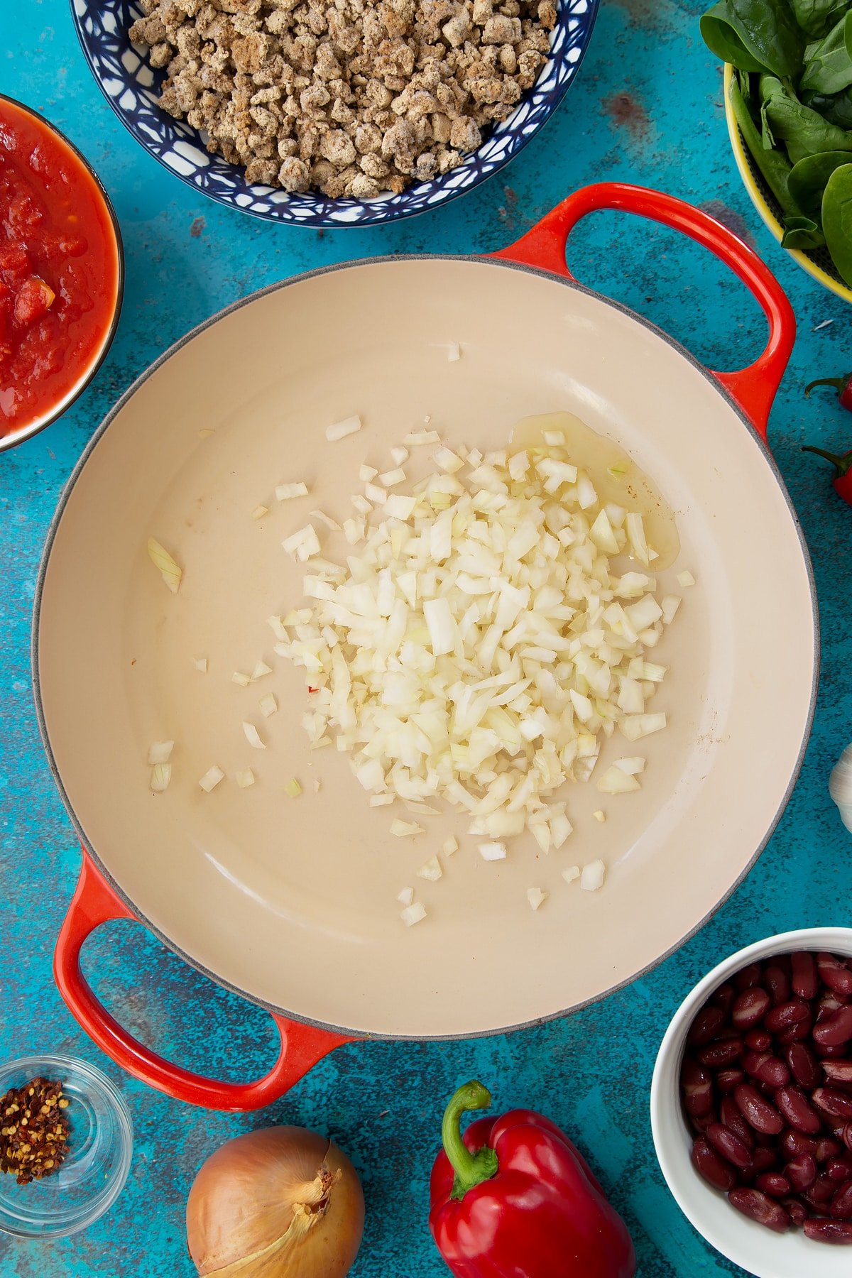 Oil and chopped onion in a pan. Ingredients to make vegetarian mince chilli surround the pan.