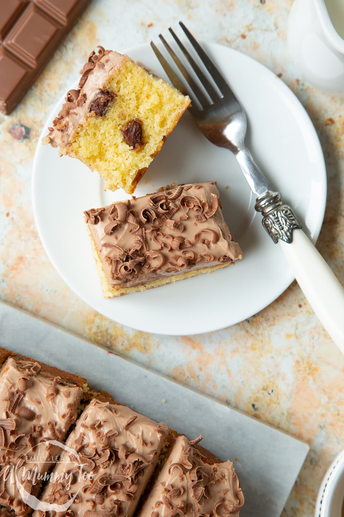 Two squares of chocolate chip tray bake on a white plate with a fork. 