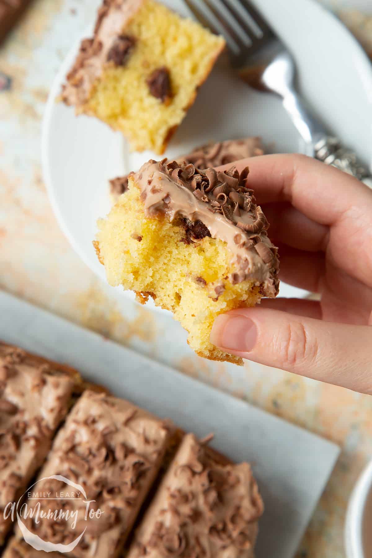 Hand holding a piece of chocolate chip tray bake with a bite taken out of it.