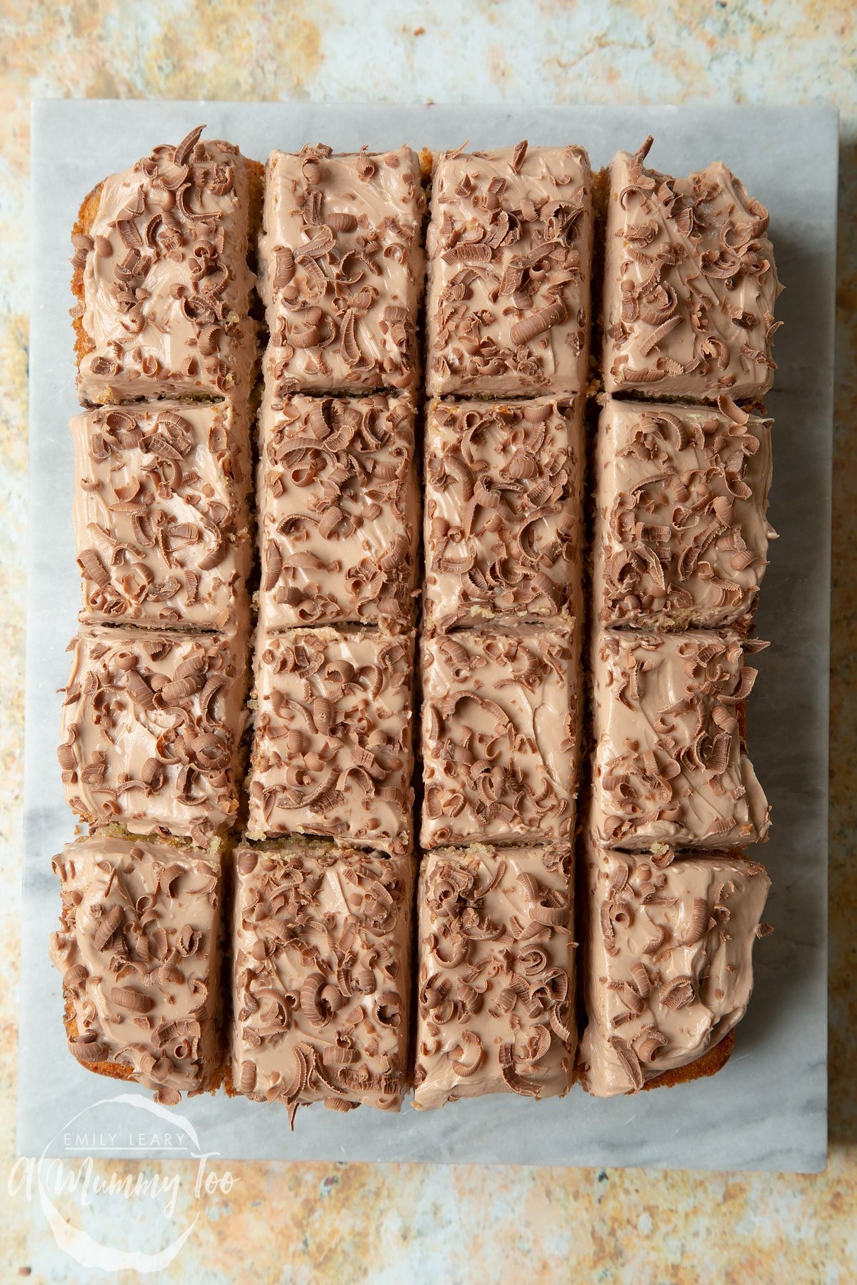 Freshly decorated chocolate chip tray bake on a marble board. The cake is cut into 16 pieces.