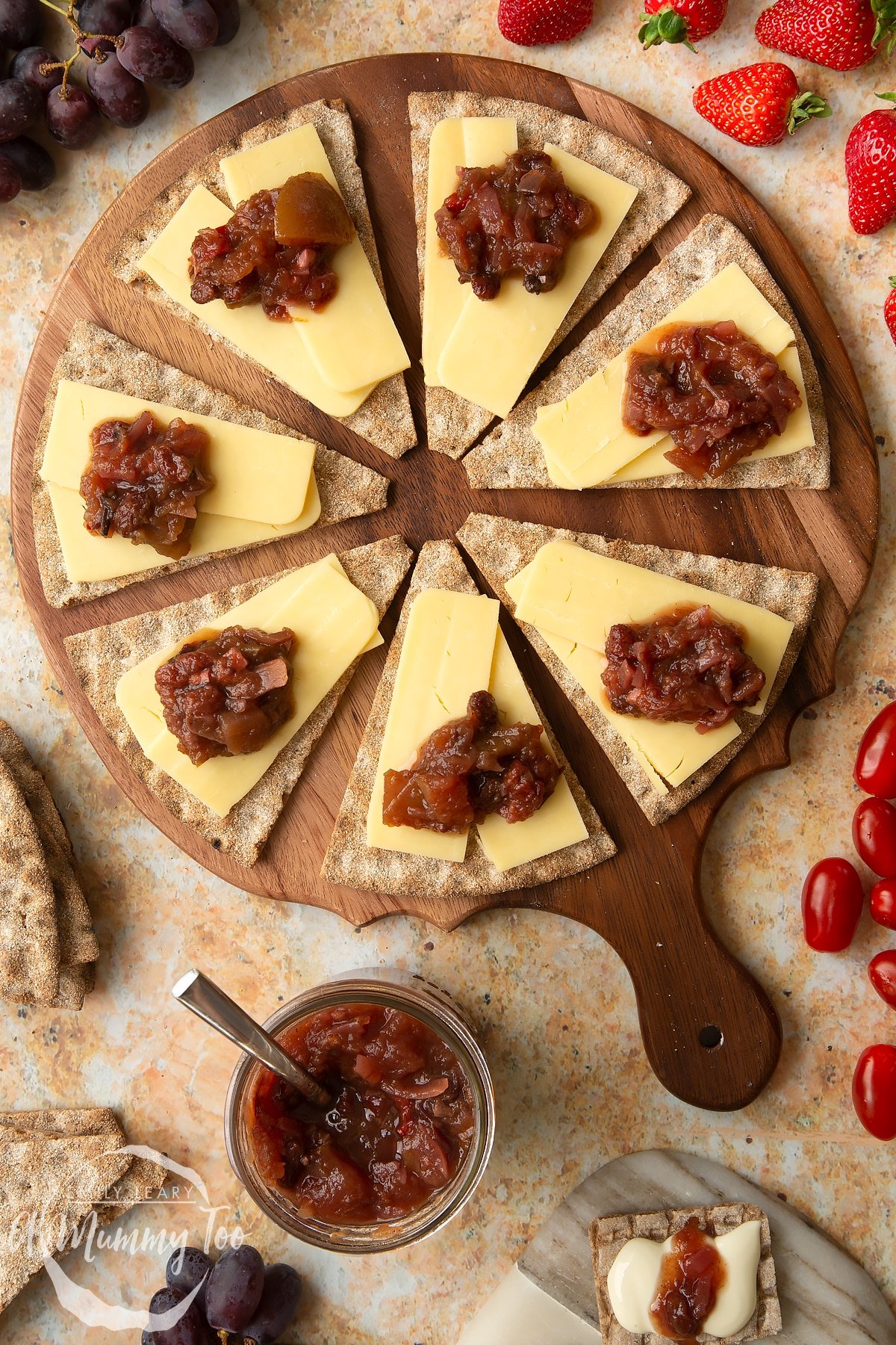 Triangular crackers topped with cheese slices and a fruit chutney recipe on a wooden board.