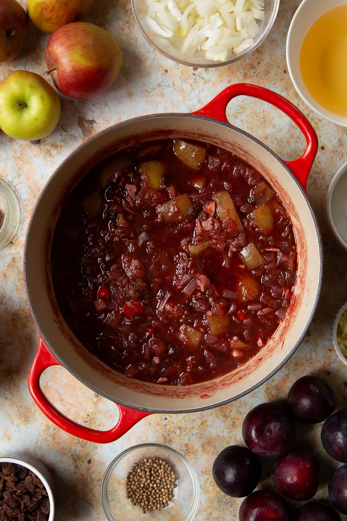 Almost cooked fruit chutney in a large pan. Ingredients to make a fruit chutney recipe surround the pan.