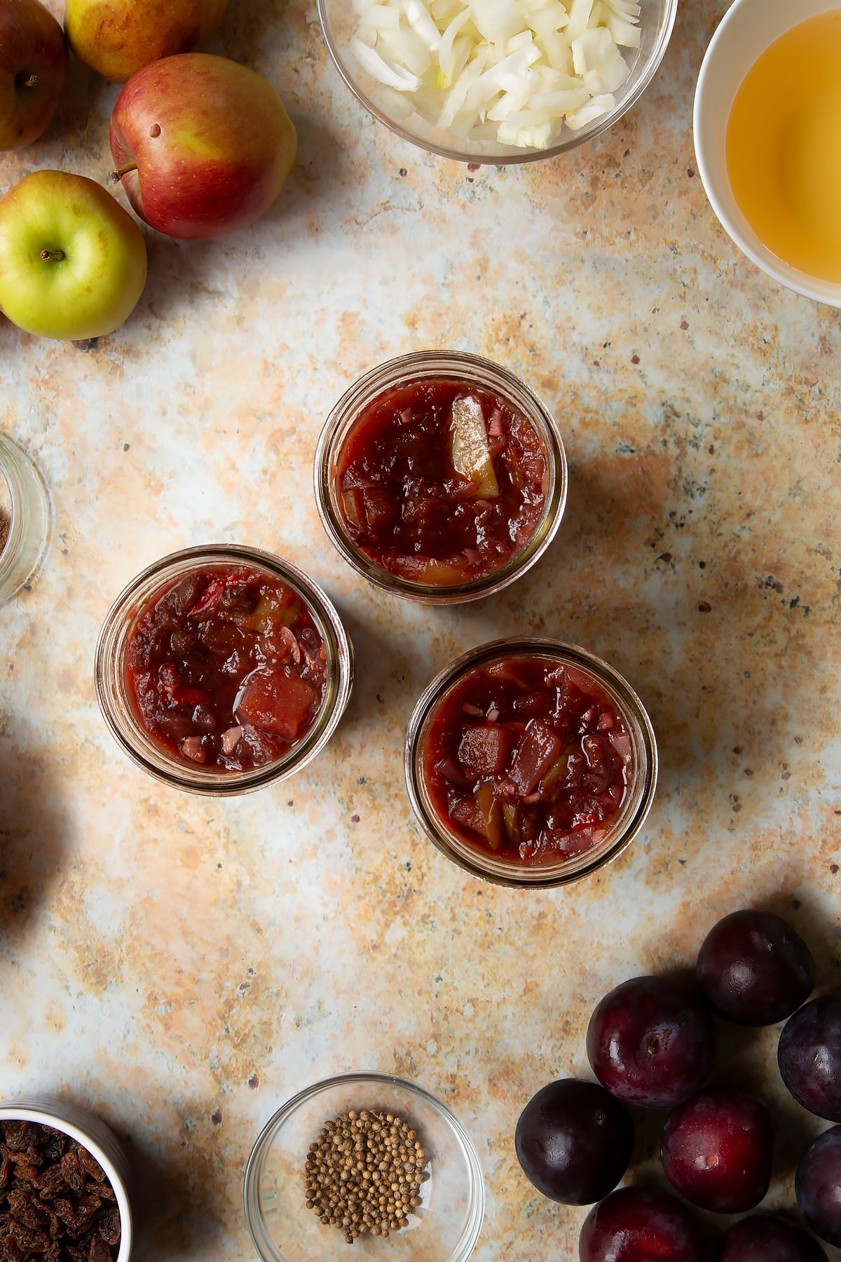 Fruit chutney in three jars. Ingredients to make a fruit chutney recipe surround the pan.