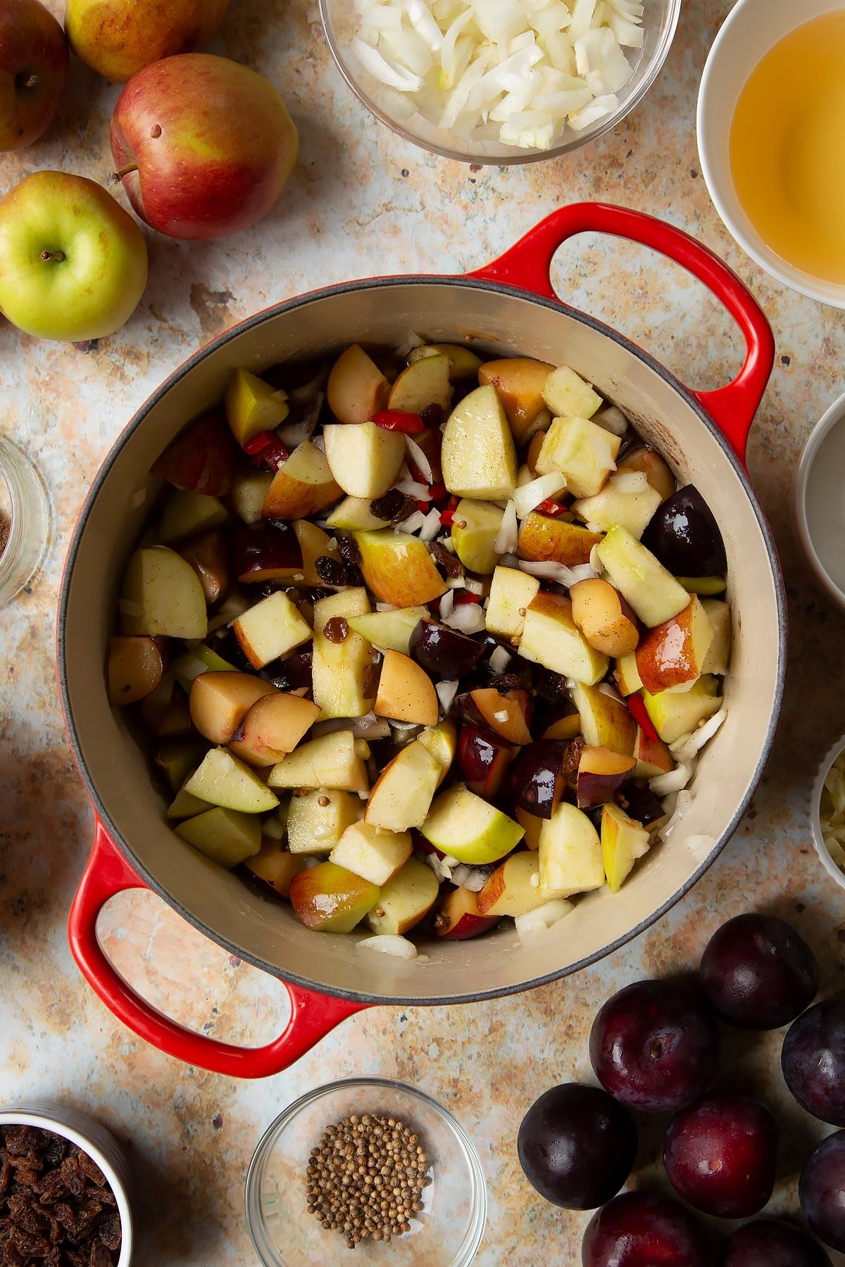 Fruit, spices, vinegar and water in a large pan. Ingredients to make a fruit chutney recipe surround the pan.