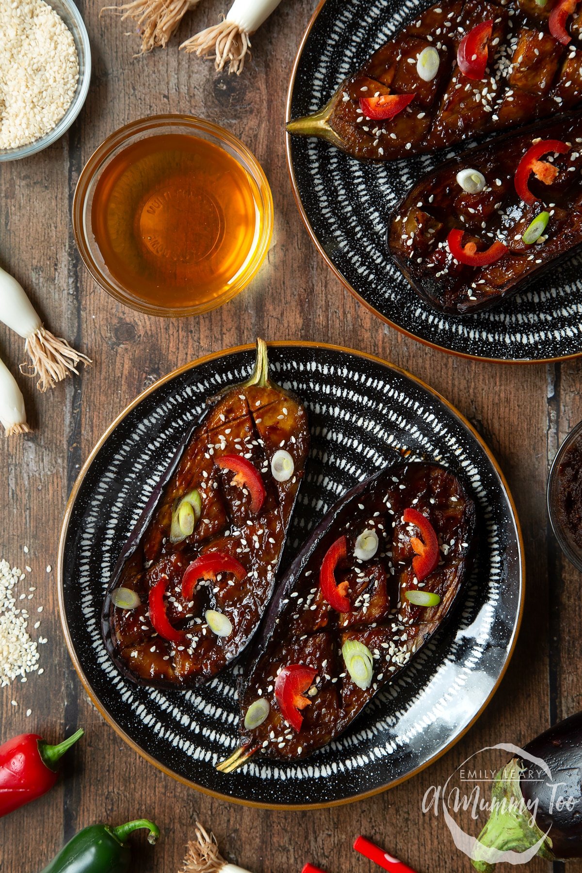 Two slices of miso aubergine on a plate, topped with chilli, spring onions and sesame seeds.