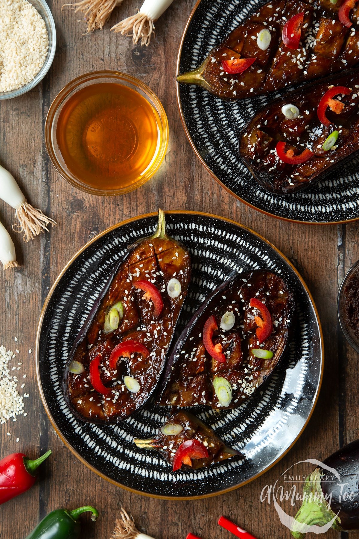 Two slices of miso aubergine on a plate, topped with chilli, springs onions and sesame seeds. A piece has been sliced off.