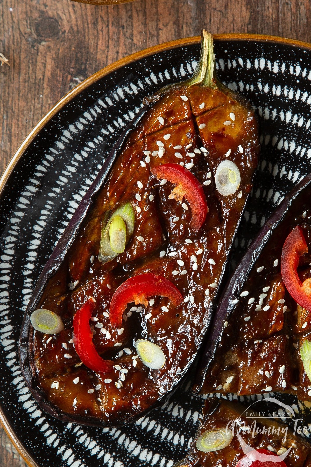 Close up of miso aubergine on a plate, topped with chilli, spring onions and sesame seeds.