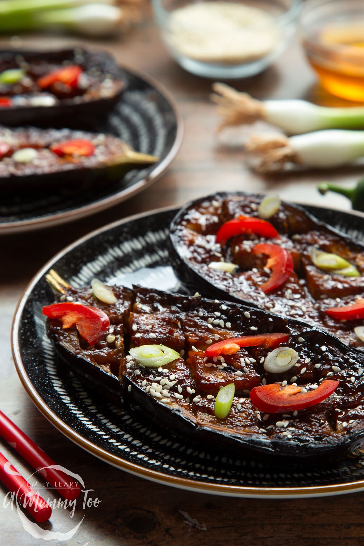 Miso aubergine on a plate, topped with chilli, springs onions and sesame seeds. Another plate shows in the background.