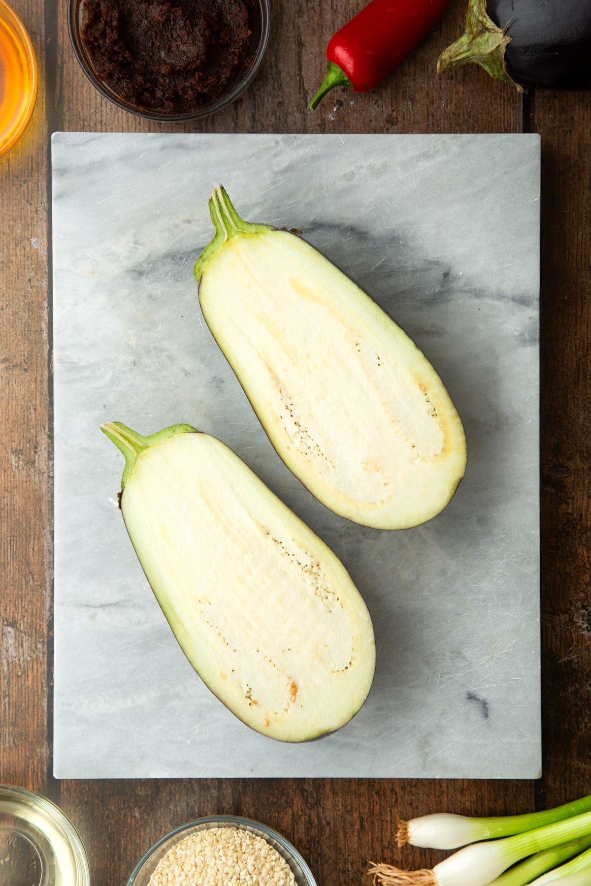 Aubergine sliced in half on a board. Ingredients to make miso aubergine surround the board.