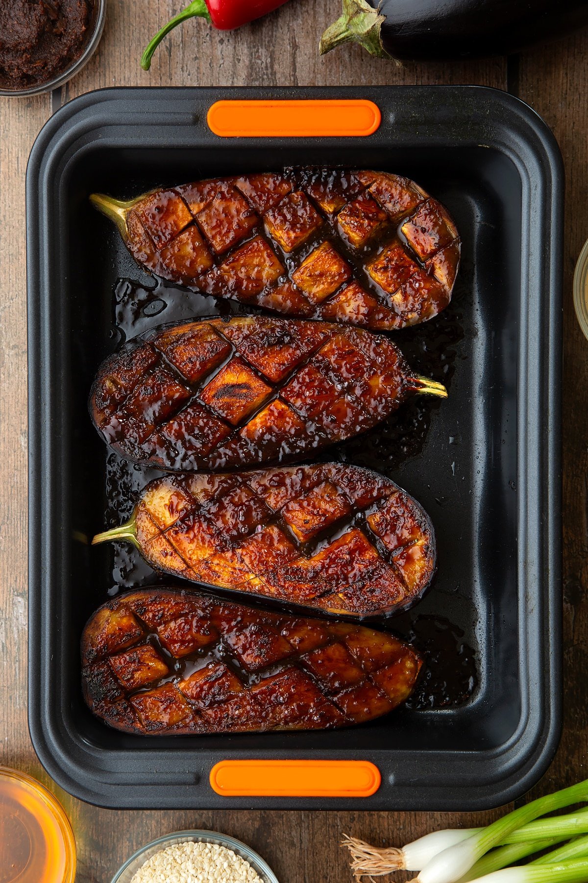 Aubergine halved covered with a miso glaze and grilled. Ingredients to make miso aubergine surround the tray.
