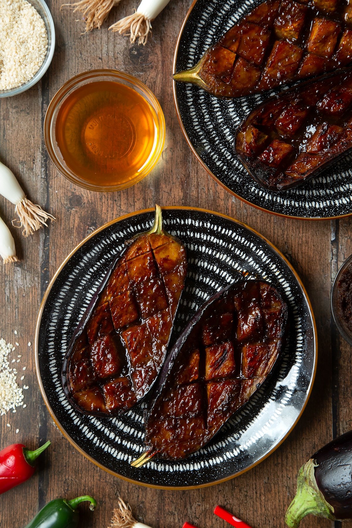 Aubergine halves with a miso glaze on a plate. Ingredients to make miso aubergine surround the tray.