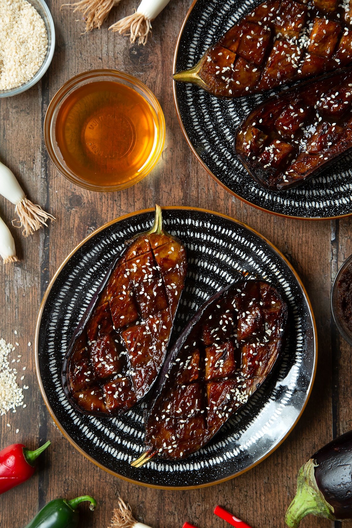 Aubergine halves with a miso glaze and sesame seeds on a plate. Ingredients to make miso aubergine surround the tray.