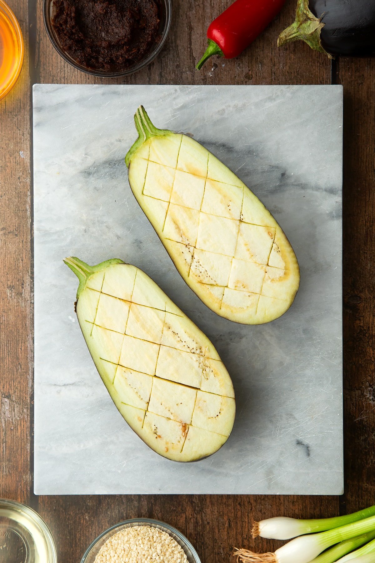 Aubergine sliced in half and scored on a board. Ingredients to make miso aubergine surround the board.