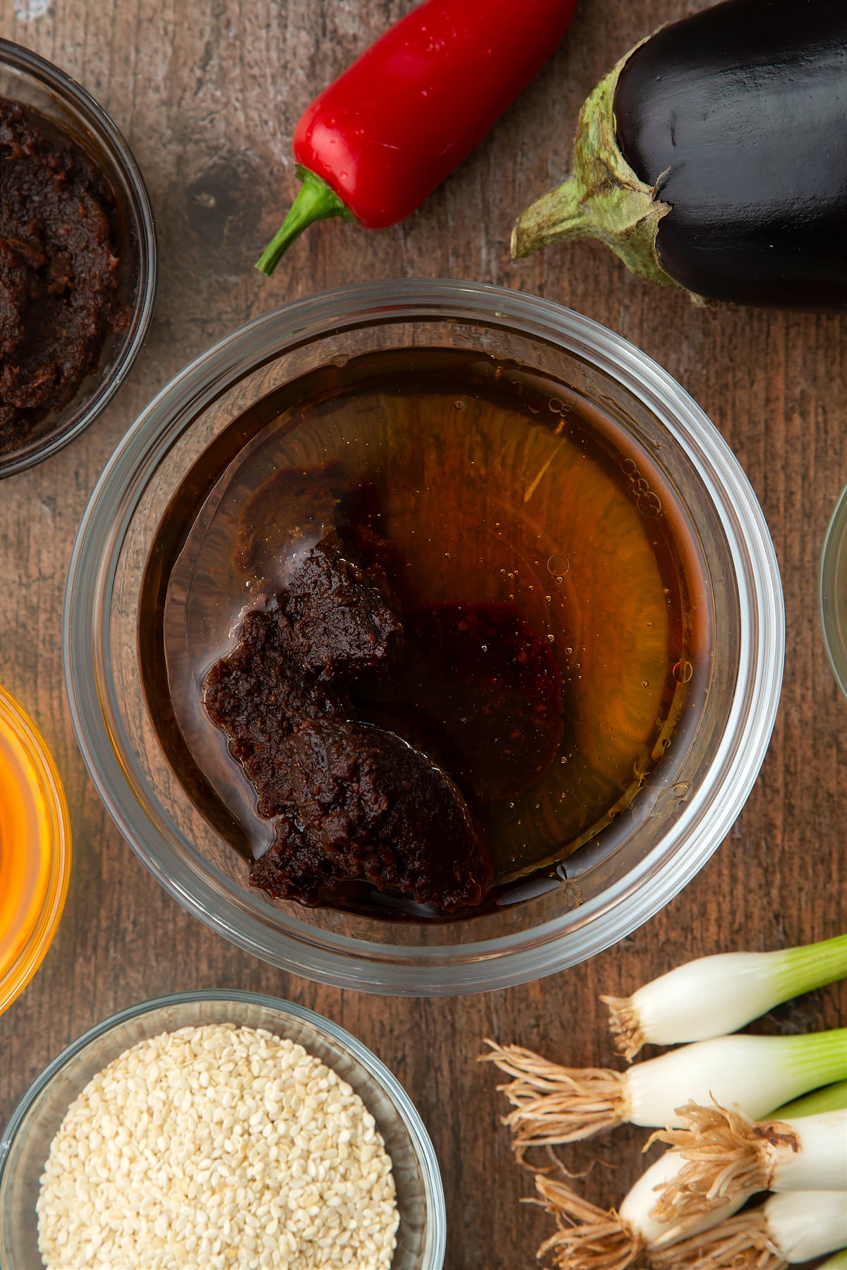 Oil, miso, honey and mirin in a bowl. Ingredients to make miso aubergine surround the bowl.