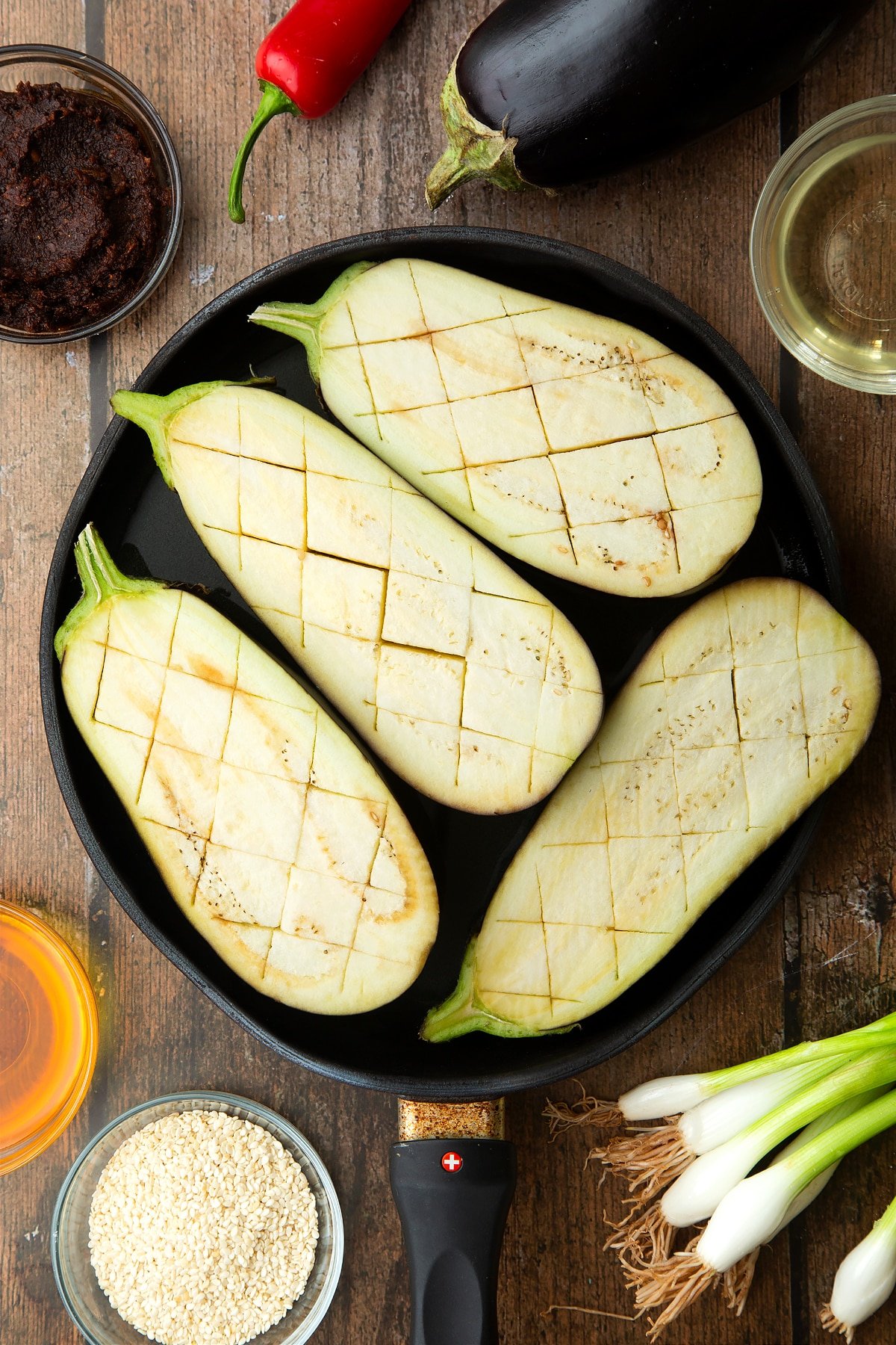 Scored aubergine halves, flesh side up in a pan. Ingredients to make miso aubergine surround the pan.