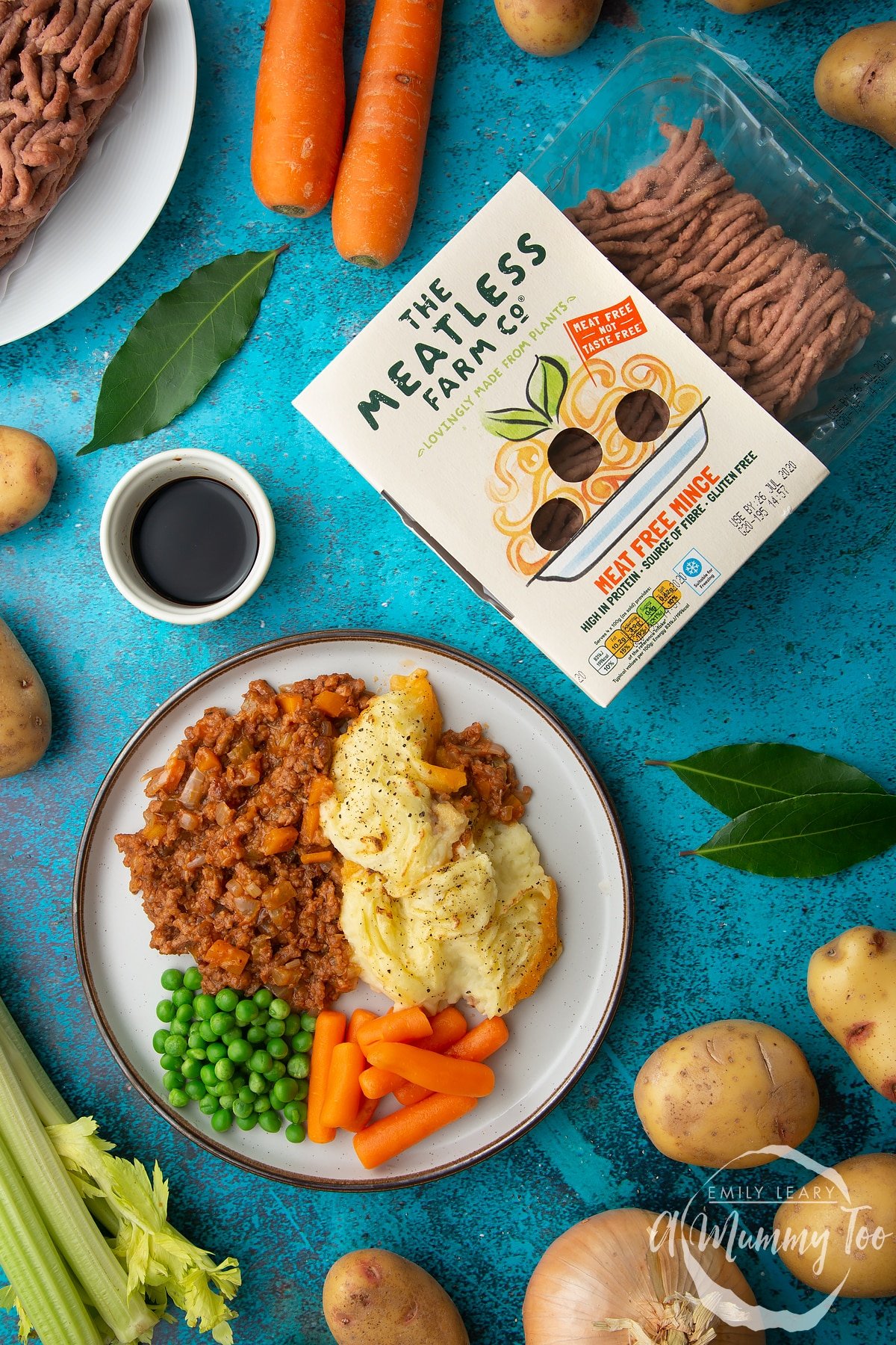 Vegan cottage pie served on a plate with peas and carrots. To the side is a packed of The Meatless Farm Co Meat Free Mince.