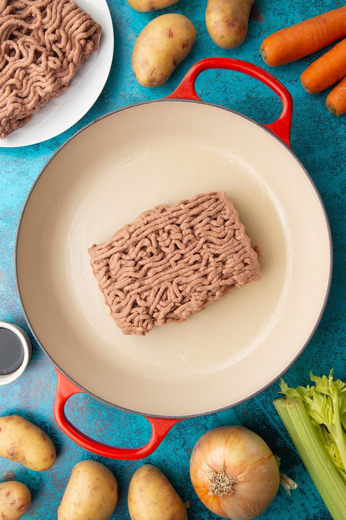 A block of meat free mince in a large pan. Ingredients to make vegan cottage pie surround the pan.